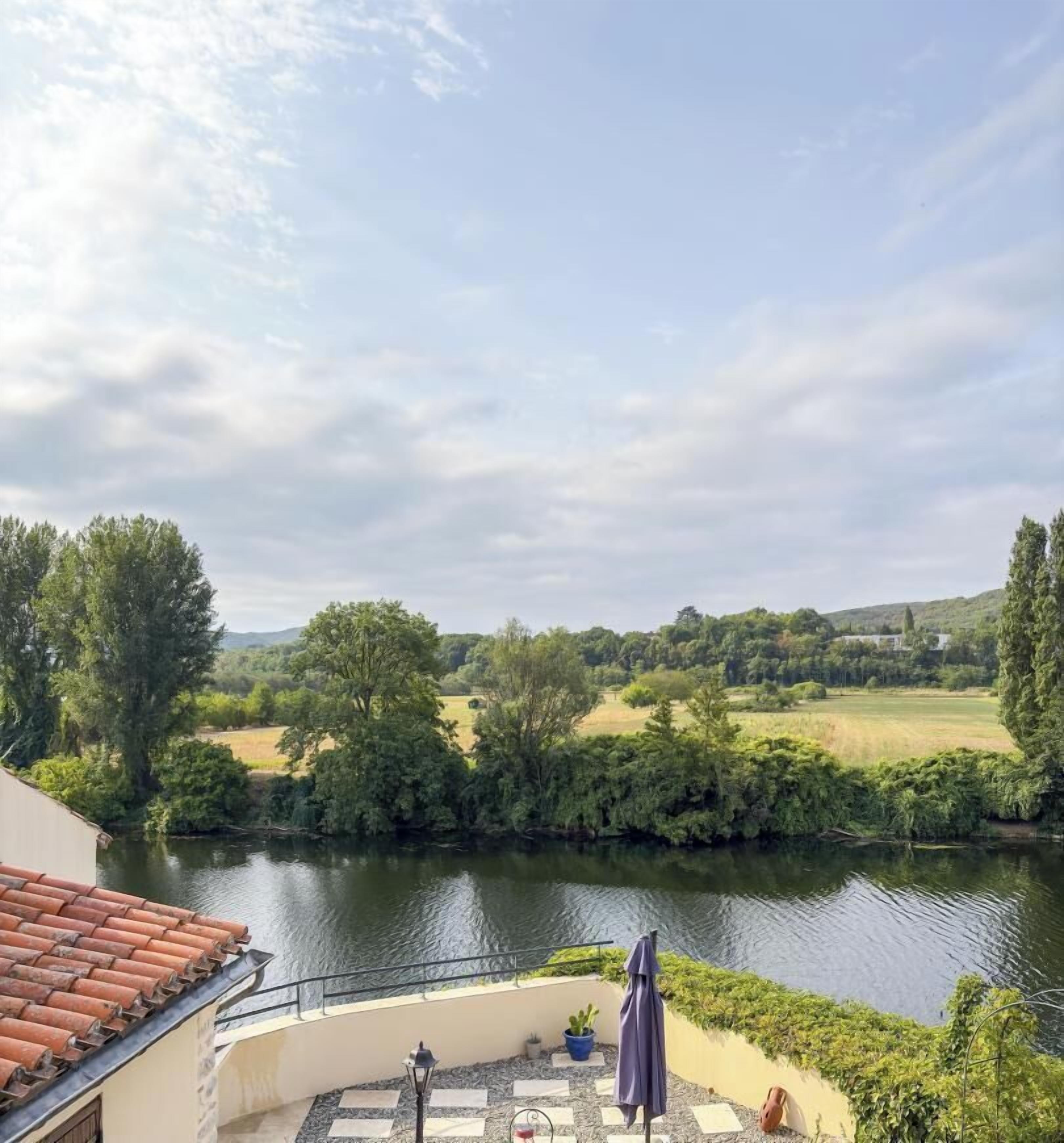 A riverside terrace with a view of a river, trees, and a distant landscape.
