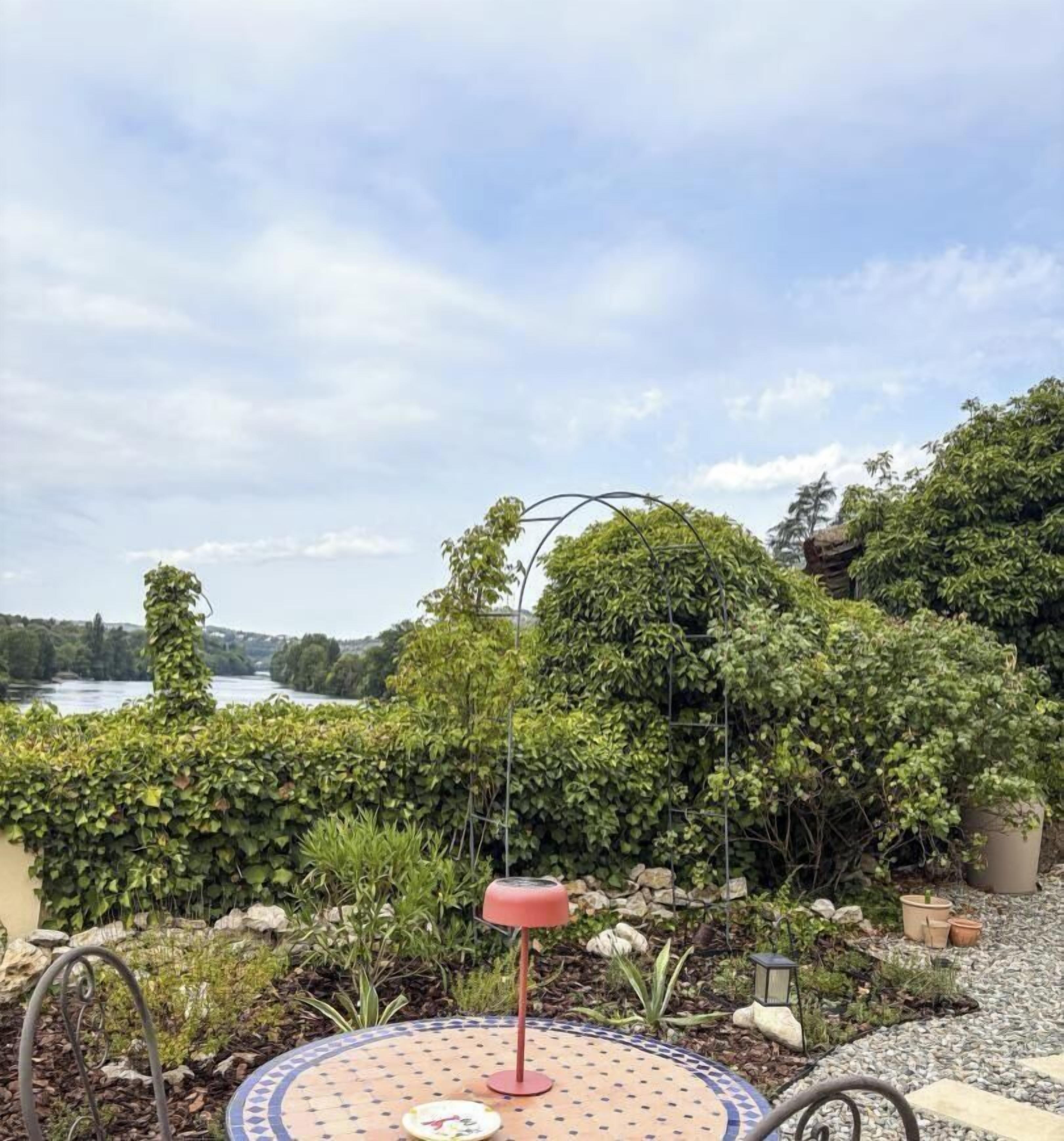 Un jardín con una mesa redonda, una lámpara roja y vista a un lago.