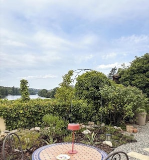Un jardin avec une table ronde, une lampe rouge et une vue sur un lac.