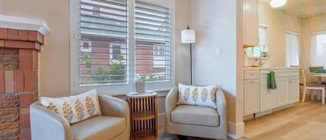 A living room with two sofas, a small round table, and a lamp. There is a kitchen area with cabinets and a countertop visible.