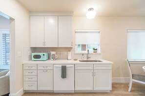 A modern kitchen with white cabinetry, a built-in microwave, a coffee maker, and a window with blinds. - Peaceful UNR Retreat 2 Bed 2 Bath (Reno)