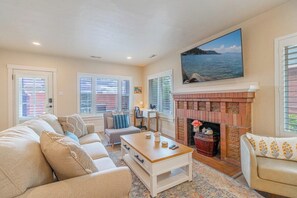 A living room with a fireplace, a sofa set, a coffee table, and a painting of a landscape. - Peaceful UNR Retreat 2 Bed 2 Bath (Reno)