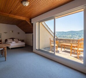 Een slaapkamer met een grote schuifpui die uitkomt op een terras met houten meubels.