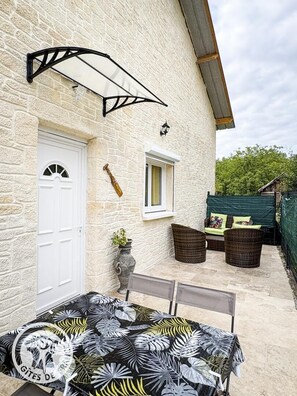A stone building with a white door, a window, and a patio area with outdoor furniture. - Gîtes de France® - French Overseas Departments and Territories (SAINT SOZY)