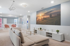 Ein modernes Wohnzimmer mit einem beigefarbenen Sofa, einem Glastisch und einer weißen Unterhaltungseinheit mit Dekorationselementen.