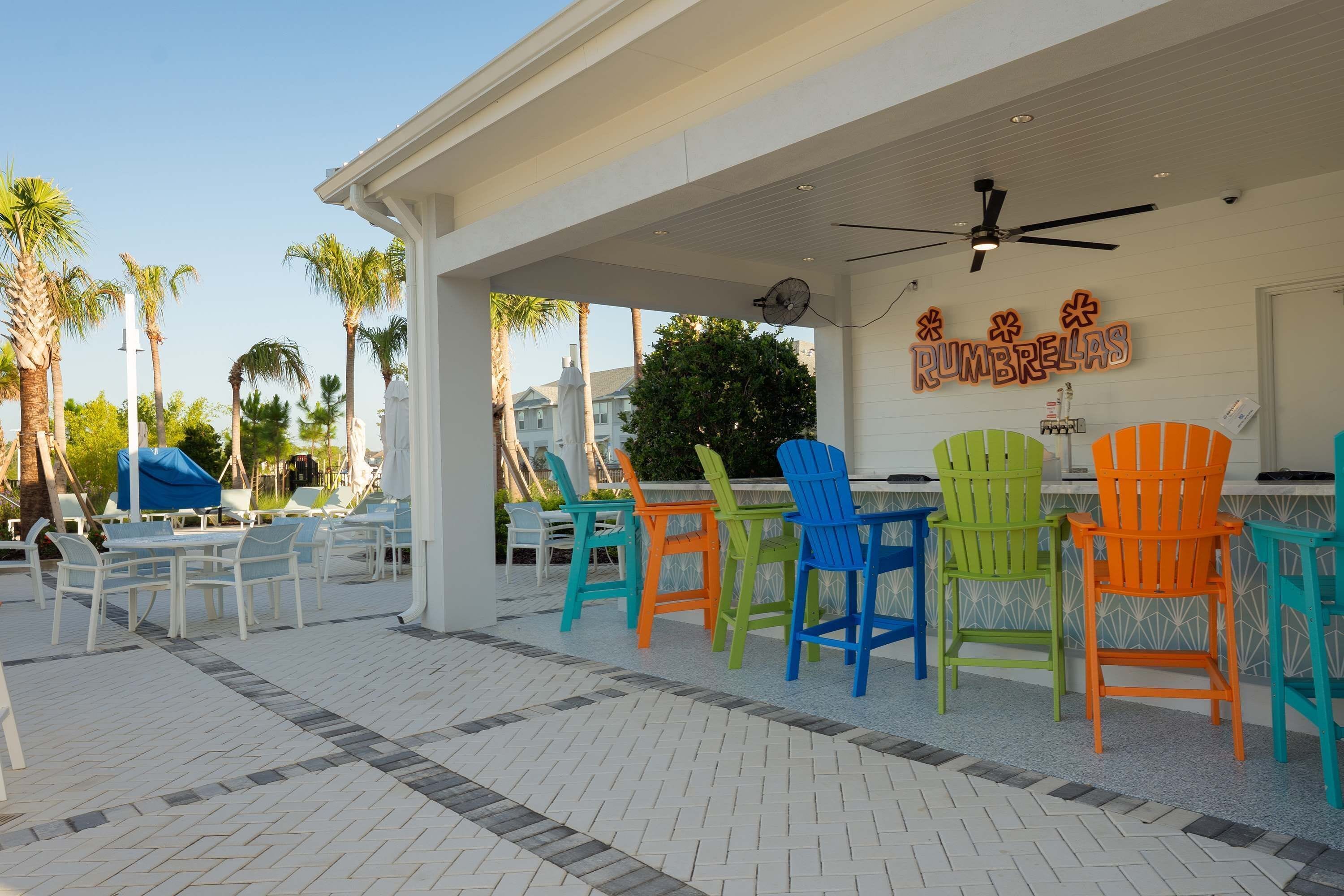 A covered outdoor seating area with colorful chairs and a ceiling fan.