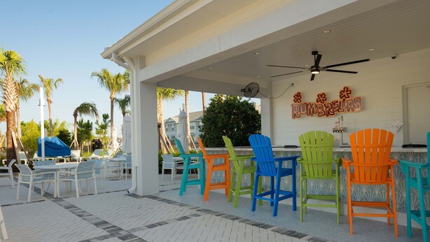 A covered outdoor seating area with colorful chairs and a ceiling fan. - Spacious Family Escape Pool Game Room (Clermont)