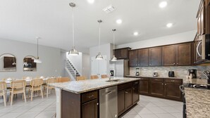 A modern kitchen with dark wood cabinets, a granite countertop, stainless steel appliances, and pendant lighting. - Spacious Family Escape Pool Game Room (Clermont)