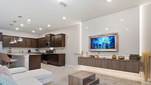 A modern kitchen with dark wood cabinets, stainless steel appliances, and a large flat-screen TV mounted on the wall. - Spacious Family Escape Pool Game Room (Clermont)