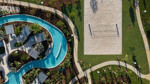 An aerial view of a resort with a large pool, a sandy beach area, and a well-maintained lawn. - Spacious Family Escape Pool Game Room (Clermont)