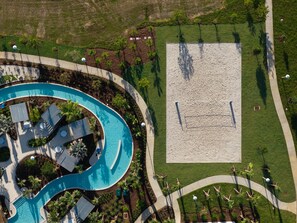 Luftaufnahme eines Resorts mit großem Pool, Sandstrand und gepflegter Rasenfläche.