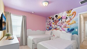 A bedroom with two single beds, a flat-screen TV, a decorative wall mural, and a window with curtains. - Spacious Family Escape Pool Game Room (Clermont)