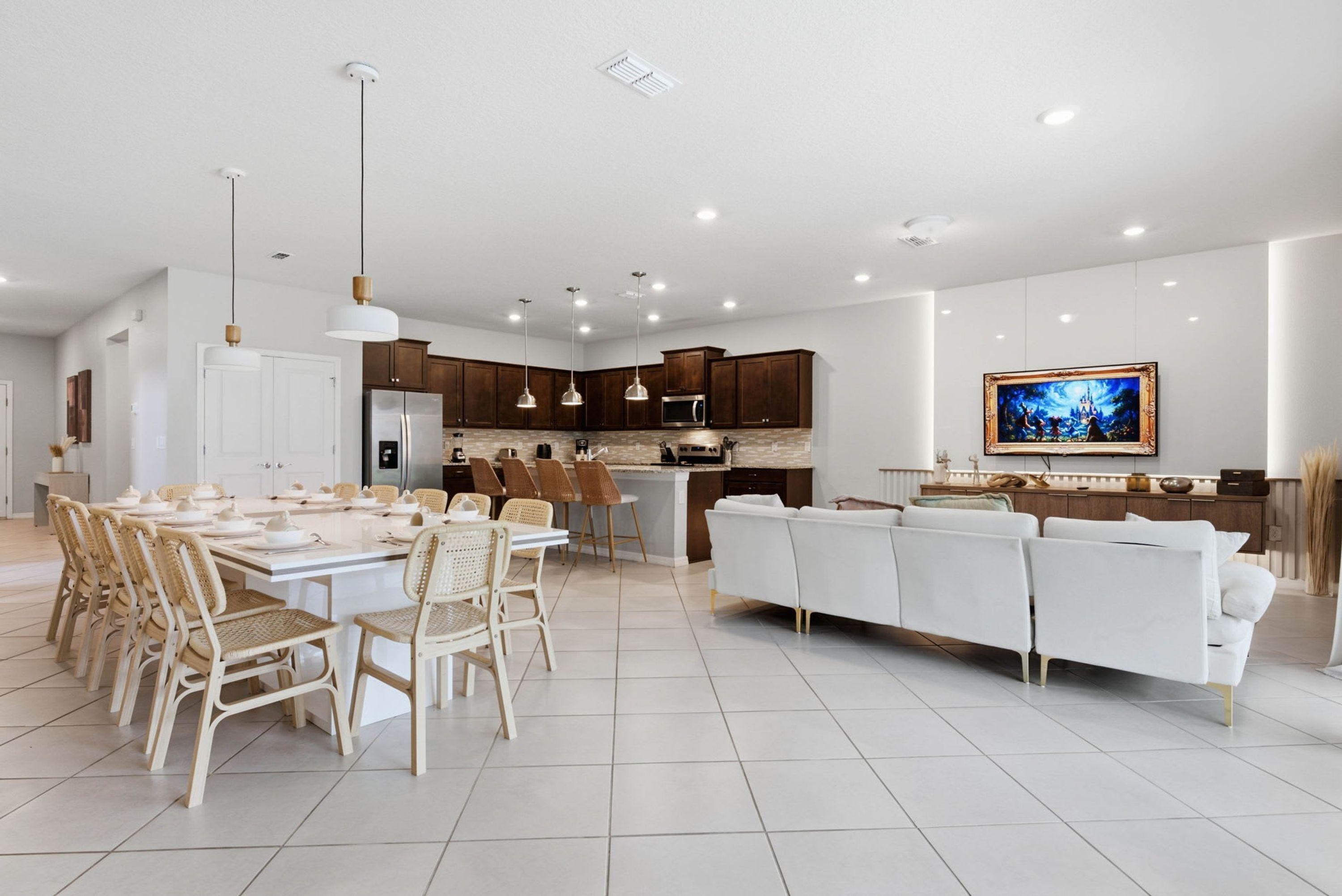 A modern kitchen with dark wood cabinets, a stainless steel refrigerator, and a dining area with wicker chairs and a white table.