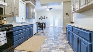 A kitchen with blue cabinets, a stove, and a dining area with a table and chairs. - Spacious 4 BR/2 BA + Grill/Firepit (San Angelo)