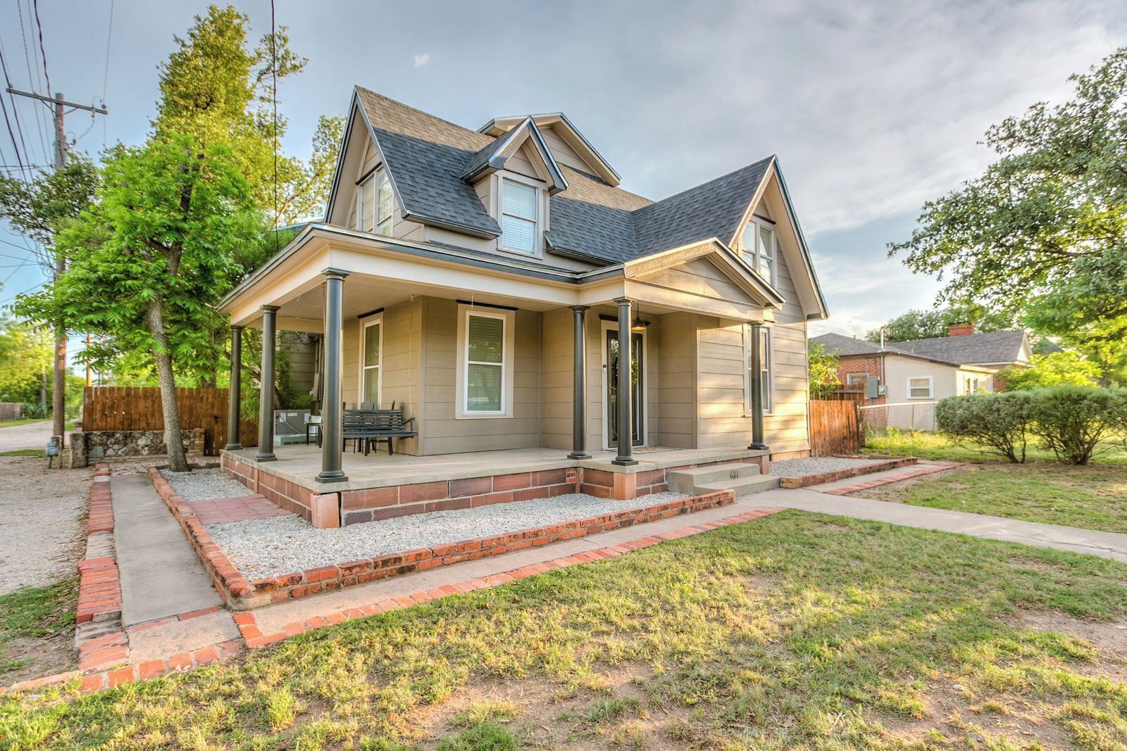 A two-story house with a covered porch, a front yard, and a wooden fence.