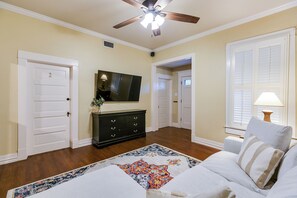 A room with a ceiling fan, a flat-screen TV, a dark-colored dresser, a patterned rug, and a white sofa with pillows. - Spacious 4 BR/2 BA + Grill/Firepit (San Angelo)