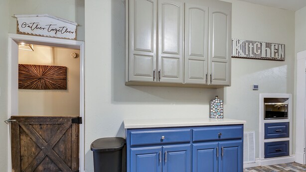 A kitchen with white cabinets, a blue countertop, and a rustic wooden door. - Spacious 4 BR/2 BA + Grill/Firepit (San Angelo)