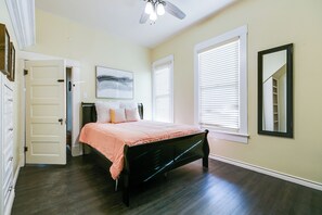 Ein Schlafzimmer mit einem Bett, einem Deckenventilator, einem Fenster mit Jalousien und einer Tür.