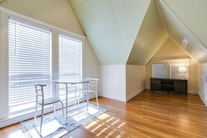 A spacious attic room with a sloped ceiling, large windows with blinds, a dining table with chairs, and a small kitchen area. - Spacious 4 BR/2 BA + Grill/Firepit (San Angelo)