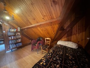 Une chambre mansardée chaleureuse avec un plafond en bois, une bibliothèque, une chaise et un lit recouvert d’une couvre-lit à motifs floraux.