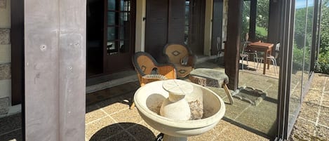 A covered patio area with a stone table and chairs, a glass enclosure, and a view of the outdoors.