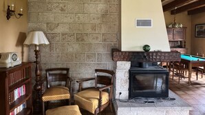 A cozy room with a stone wall, a fireplace, wooden furniture, and a billiards table.