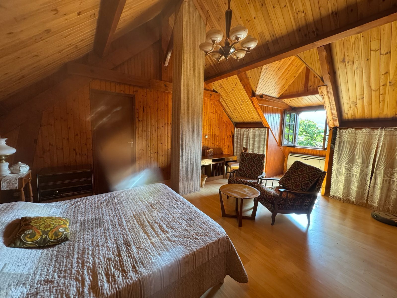 Une cabane confortable avec un lit, une chaise, une table et une fenêtre avec des rideaux.