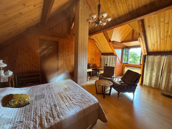 A cozy cabin with a bed, a chair, a table, and a window with curtains.