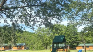Un parque infantil con tobogán y columpios, una mesa de picnic y un edificio al fondo.