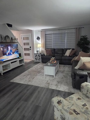 A living room with a flat-screen TV, a sofa, a coffee table, and a patterned rug. - John Boxtel Retreat – A One-of-a-Kind (Greater Napanee)