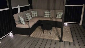 Een overdekt terras met een bank en een tafel, een kamerbreed tapijt met dessin, en een houten terras.