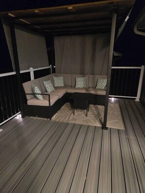 Ein überdachter Außenbereich mit einer Couch und einem Tisch, einem gemusterten Teppich und einem Holzboden.