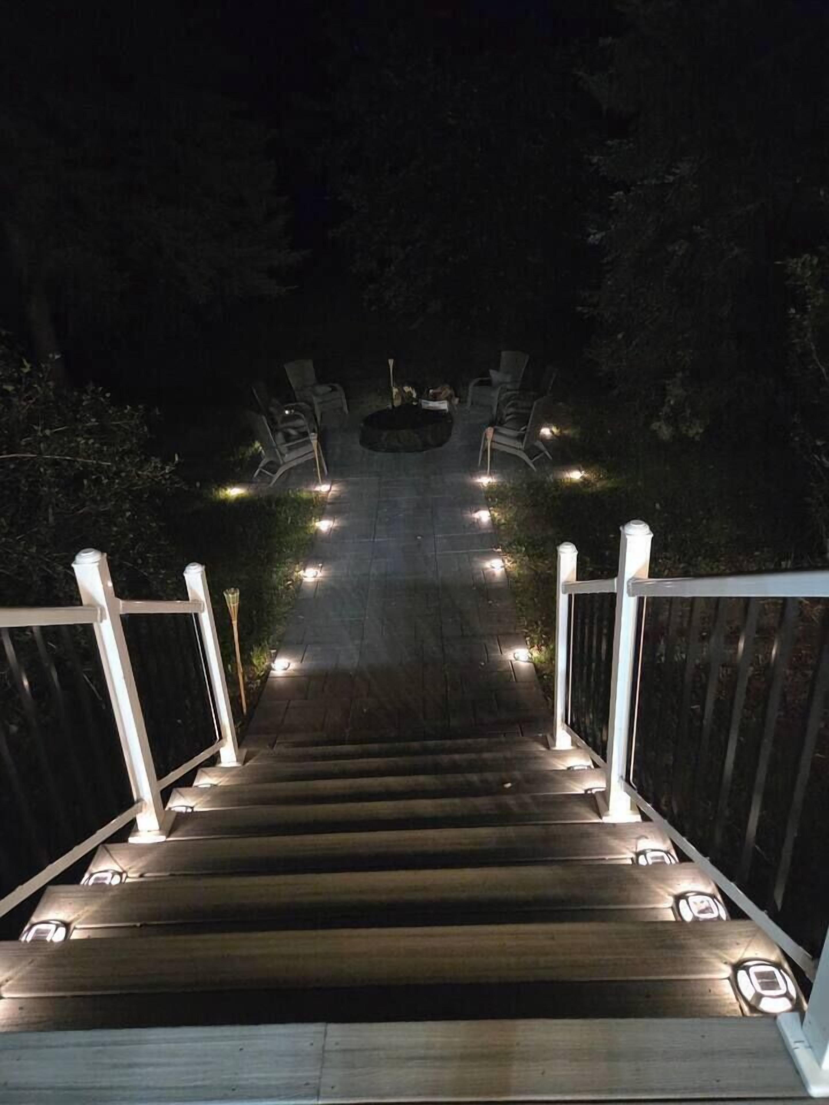 Un escalier en bois, avec des rampes et des luminaires blancs le long des marches, qui monte.