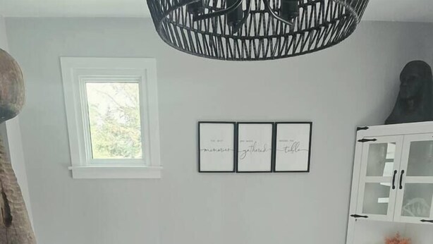 Een eethoek met een witte tafel, stoelen en een dienblad met kaarsen en bloemen. Daarboven hangt een raam en rechts staat een kast.