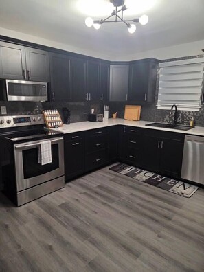 A modern kitchen with dark cabinets, stainless steel appliances, and a light-colored countertop. - John Boxtel Retreat – A One-of-a-Kind (Greater Napanee)