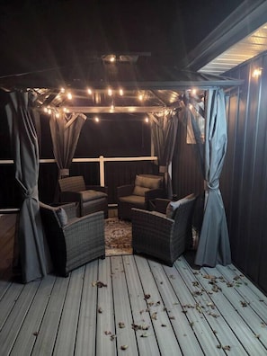 A covered outdoor seating area with wicker furniture and curtains. - John Boxtel Retreat – A One-of-a-Kind (Greater Napanee)