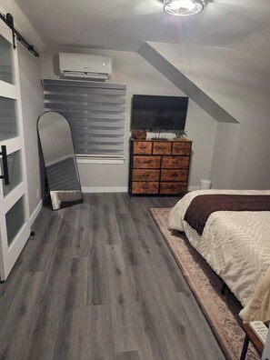 A bedroom with a bed, dresser, mirror, and air conditioning unit. - John Boxtel Retreat – A One-of-a-Kind (Greater Napanee)