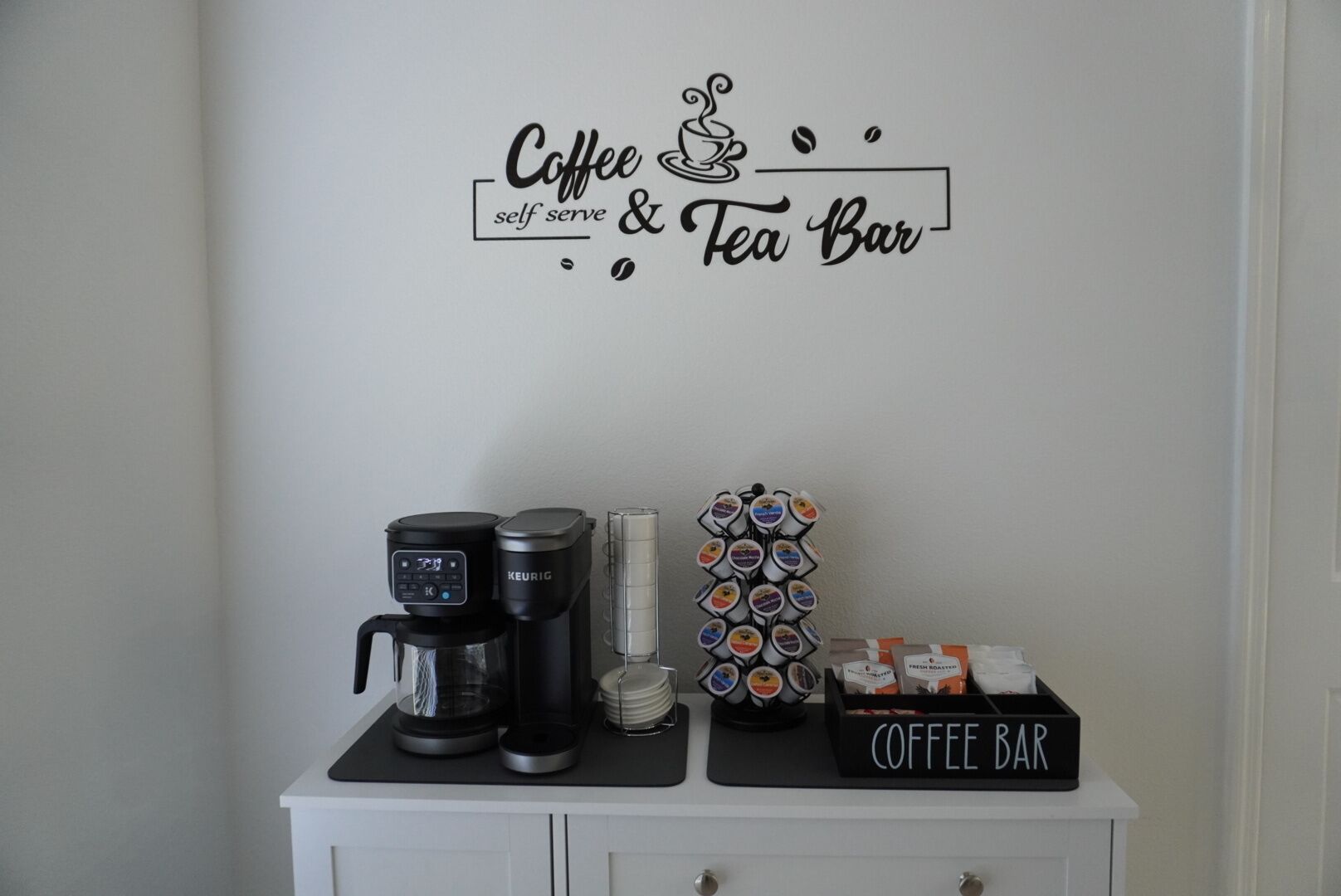 Ein Kaffee- und Tee-Bereich mit einer Kaffeemaschine, einem Tee-Spender und einem Schild für die Kaffeebar.