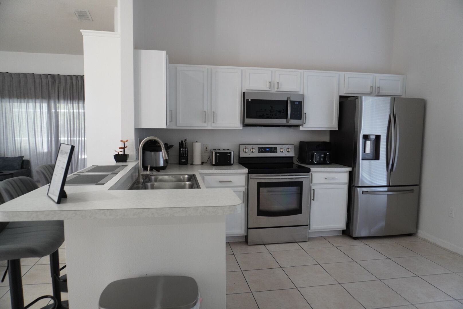 A modern kitchen with white cabinets, stainless steel appliances, and a bar area with stools.