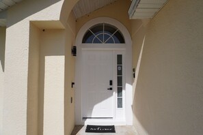 A white door with a glass panel, a doormat, and a small window above the door. - Pool home near Disney with Game Room + EV Charger (Davenport)