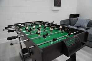 Een tafelvoetbaltafel in een kamer met een grijze bank en een witte bakstenen muur.
