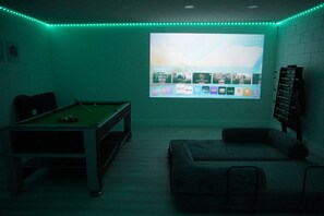 Een kamer met een pooltafel, een bank en een scherm waarop streamingdiensten worden vertoond.