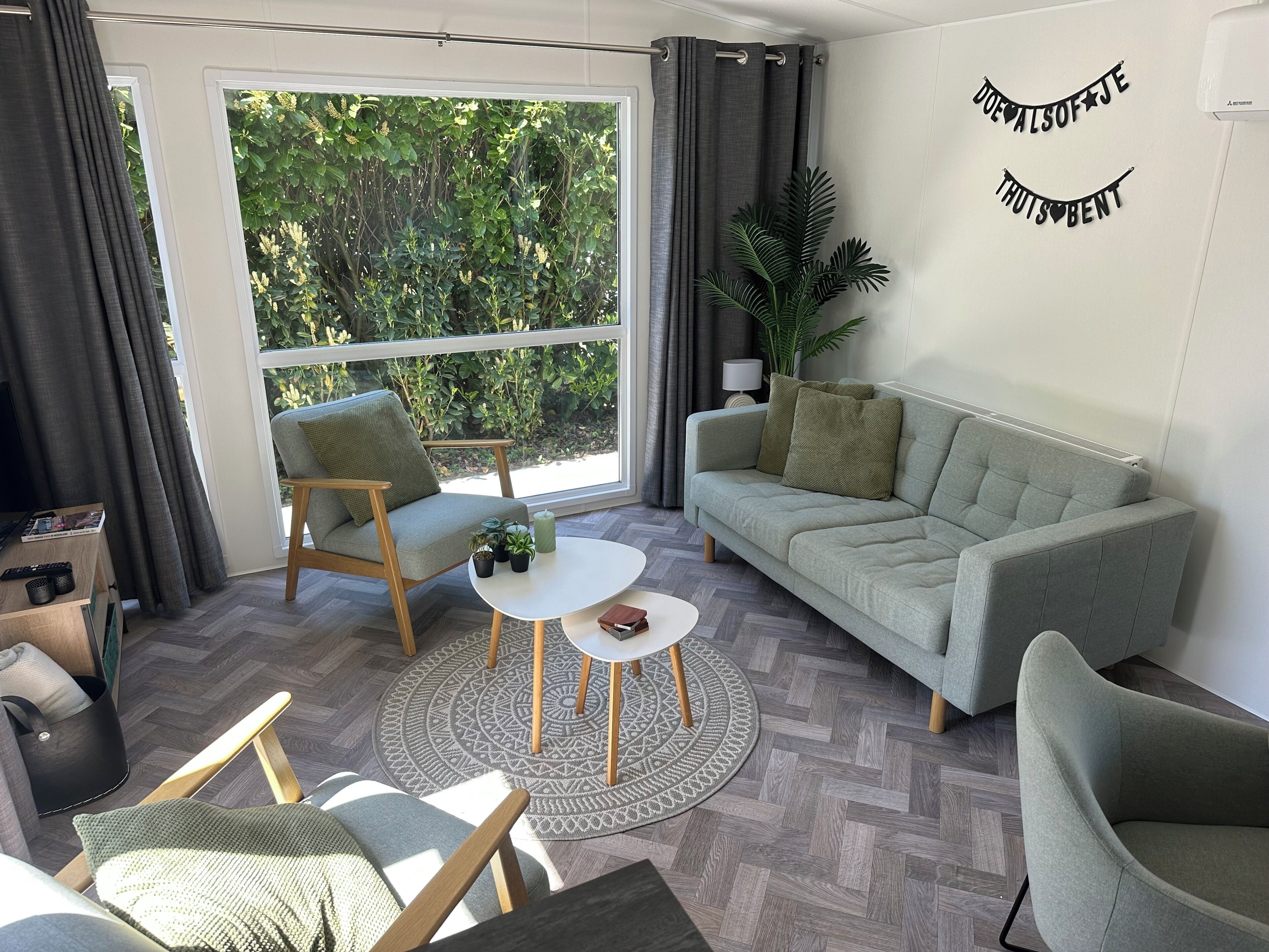 Una sala de estar moderna con sofá, sillas, una mesa de centro y vistas al exterior con vegetación.