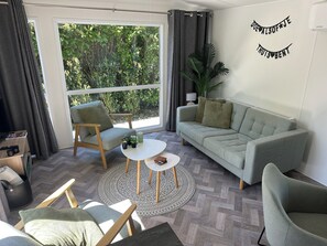 Ein modernes Wohnzimmer mit Sofa, Sesseln, einem Couchtisch und Blick auf Grünflächen außerhalb.