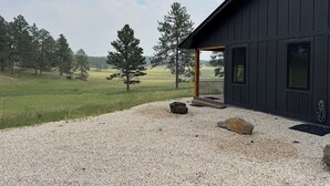 Um edifício moderno com fachada escura, entrada por um caminho de cascalho e um campo gramado com árvores ao fundo.