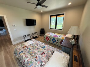 A bedroom with a large bed, a smaller bed, a desk with a lamp, a chair, a TV, and a window with a view. - New build cabin with AC on 20+ acres outside Custer (Custer)