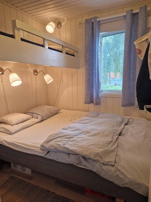 A bunk bed with two bedside lamps, a window with curtains, and a bed with striped bedding.