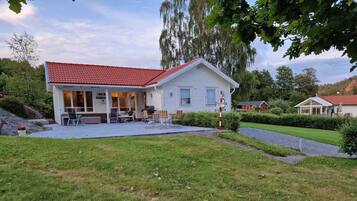 Une maison d’habitation avec un toit recouvert de tuiles rouges, un patio abrité et une pelouse bien entretenue.