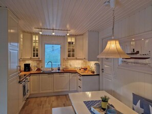 A kitchen with white cabinets, a wooden countertop, a sink, and a window with blinds.