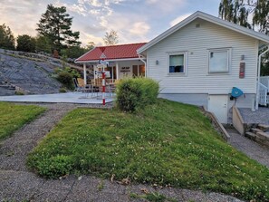 A single-story building with a red-tiled roof, a covered outdoor seating area, and a gravel driveway.